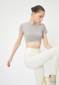 Top atletico grigio a maniche corte e design incrociato, abbinato a leggings bianchi a vita alta e sneaker grigie con suola beige.