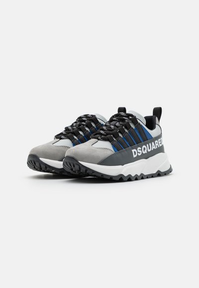 Sneakers atletici grigi e neri con materiali in rete e scamosciato, dotati di accenti blu, suole bianche spesse e un dettaglio del logo ben visibile.