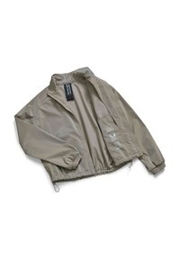 Beige lichte jas met een staande kraag, elastische manchetten en een trekkoord aan de onderkant. Bevat bedrukte logo's aan de linkerkant en een label aan de binnenkant.