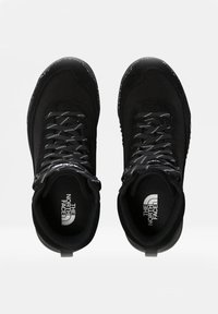 Černé turistické boty s texturovaným textilním svrškem, zesílenou špičkou, reflexními tkaničkami a logem na jazyku. Vybavené pevným gumovým podešví.