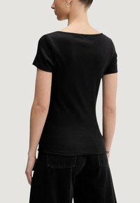 Černý žebrovaný top s krátkými rukávy a hranatým výstřihem. Látka je hladká, přiléhá těsně k tělu, s čistým, minimalistickým designem.