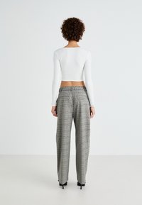 Hvit strikket langermet crop topp, kombinert med grå rutete høytlivs vide bukser med sidelommer og en avslappet passform.