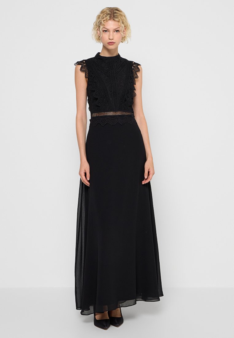 Robe maxi noire avec un corsage en dentelle à bords festonnés, une jupe transparente et un détail de taille perlé, conçue avec un col haut et sans manches.