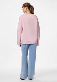 Világos rózsaszín kötött pulóver laza fazonnal, bordázott szegéllyel és hosszú ujjakkal, világoskék, magas derekú, széles szárú farmerrel párosítva.