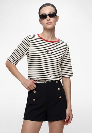 Kvinde iført sorte solbriller, en stribet skjorte med rød kant og teksten "love love love" samt sorte højtaljede shorts med guldknapper.