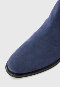 Botín de ante de color navy hasta el tobillo con puntera afilada, cuenta con una textura suave y elegante y una suela negra. Sin herrajes o embellishments visibles.