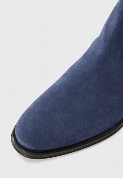 Botte de cheville en daim marine avec un bout pointu, présentant une texture lisse et élégante et une semelle extérieure noire. Pas de matériel ou d'ornements visibles.