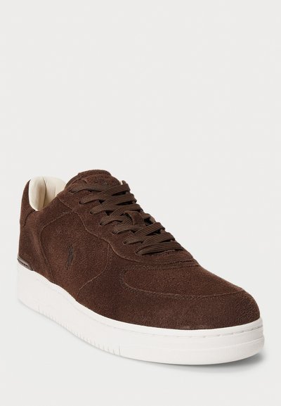 Sneaker in suede marrone con lacci marrone scuro, suola bianca e logo inciso in modo sottile sul lato, mostrato da un angolo frontale a tre quarti.