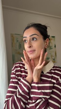 Bordeauxrode en witte gestreepte shirt met lange mouwen en een witte kraag. Persoon raakt hun gezicht aan, met een effen achtergrond en zacht licht.