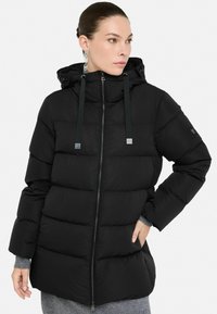 Čierna prešívaná bunda s kapucňou, so zapínaním na zips, nastaviteľnou kapucňou a kontrastnými popruhmi. Vyznačuje sa elegantnou, hladkou textúrou.
