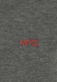 Grijze gebreide stof met opvallende rode geborduurde letters "M c G." Gladde textuur met een gelijkmatige steekpatroon en geen extra versieringen.