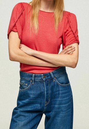 Rood topje met korte mouwen, textuurrijke pofmouwen en decoratieve rand, gecombineerd met hooggetailleerde blauwe spijkerbroek met klassieke pasvorm.