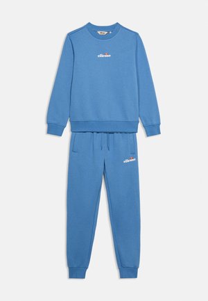Синя суитшърт и комплект панталони с лого ellesse в бяло на гърдите и лявото бедро, показани на обикновен фон.