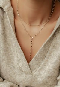 Collares de oro en capas con diseños variados, incluido un estilo lariat, que presentan eslabones delicados y un acabado suave sobre un suéter claro.