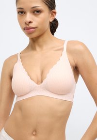 Ασύρματη σουτιέν σε ανοιχτό ροζ χρώμα με κυματιστές άκρες, υφασμάτινη υφή, βαθύ ντεκολτέ σε σχήμα V και στενές ρυθμιζόμενες τιράντες.