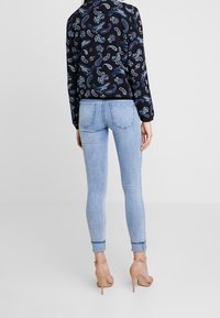 Smala jeans i ljusblå denim, i kombination med en svart skjorta med paisleymönster. Jeansen har uppvikta ben och bakfickor.