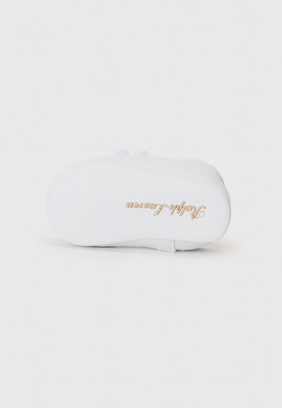 Semelle de chaussure blanche avec une texture lisse, présentant un logo de marque doré et de petites touches de violet près du talon. Design simple et minimaliste.