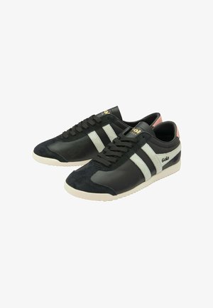 Zapatillas negras con un upper de cuero y gamuza, rayas blancas y un acento rosa en el talón. La suela texturizada y los cordones completan el diseño.