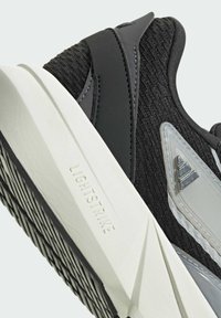 Čierne atletické topánky s textúrovaným zvrškom, svetlošedými akcentmi a bielou gumovou súšou. Na strednej podrážke sa nachádza značka "LIGHTSTRIKE".