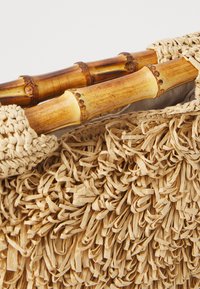 Geflochtener Strohhandschuh mit einem strukturierten Fransen-Design, natürlicher beige Farbe und Bambushandles, ausgestattet mit einem weich gefütterten Innenraum.
