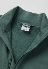 Grøn zip-up sweater med en tekstureret indvendig krave og glat yderstof. Har et mærke, der angiver størrelse og oprindelse.