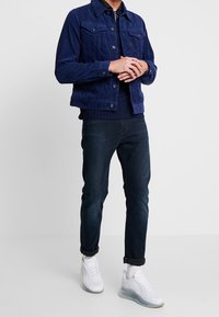 Marinblå kordjacka med två framfickor, kombinerad med mörk denimjeans och vita sneakers med genomskinlig sula. Avslappnad klädoutfit.