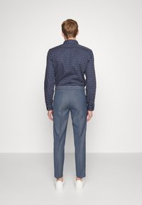 Marinblå mönstrad långärmad skjorta med hög krage, kombinerad med ljusgrå skräddarsydda byxor och vita sneakers, sedd från baksidan.