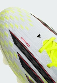 Λευκό ποδοσφαιρικό παπούτσι με κίτρινες λεπτομέρειες, διαθ έτοντας υφασμένο επάνω μέρος, μαύρες ρίγες και την επωνυμία "SPRINTWEB" κοντά στη φτέρνα.