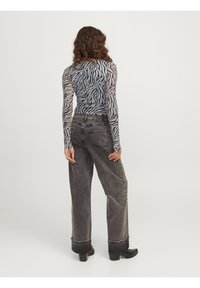 Doorzichtig langewerpshirt met zwarte en grijze zebrastripes, gecombineerd met grijze high-waisted wide-leg jeans met opgerolde zomen en zakken.