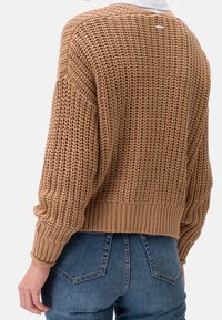 Stickad tröja i medelbrunt, med ett strukturerat mönster, sänkta axlar och ribbade muddar och nederkant. Tagg synlig på baksidan.