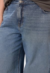 Light blue denim jeans featuring a relaxed fit, five-pocket style, visible stitching, and a metal button closure at the waistband.