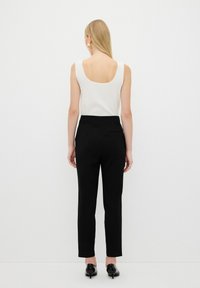Zwarte broek met een rechte snit en een gladde textuur, gecombineerd met een witte ribbelige tanktop met een ronde achterkant.