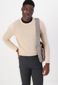 Beige gebreide trui met textuur en ronde halslijn, gecombineerd met donkere broeken. Grijze schoudertas met verstelbare band. Eenvoudig ontwerp, casual uitstraling.