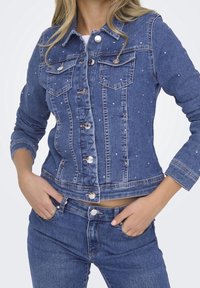 Denim jacket with a fitted design, light blue color, and embellished with small studs. Features two chest pockets and silver buttons.