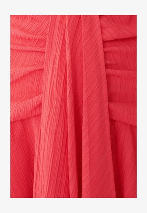 Koralová plisovaná látka, která ukazuje texturu s jemnými vertikálními liniemi. Materiál elegantně splývá ve vrstvených záhybech. Žádné viditelné kovové prvky ani ozdoby.