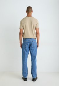 T-shirt beige con collo a costine abbinato a jeans in denim blu con tasche posteriori e taglio dritto, indossato con scarpe nere.