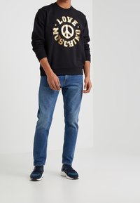 Svart sweatshirt med guldfärgade bokstäver "LOVE MOSCHINO" och en fredssymbol. Matchas med blå jeans och marinbl�å sneakers med svarta detaljer.