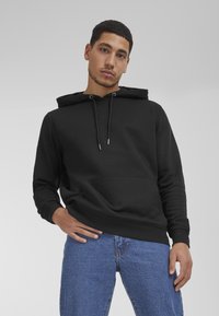 Black hoodie made from soft fabric, featuring a front pocket, adjustable drawstring hood, and ribbed cuffs. Paired with blue denim jeans.