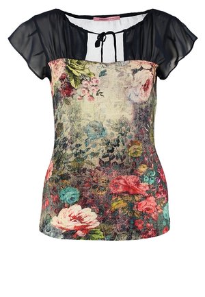 Mujer con blusa floral de mangas negras transparentes, jeans ajustados azules, botines marrones y un bolso de hombro con flecos color marrón claro.