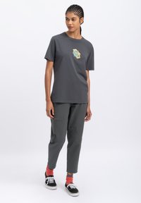 Grijze katoenen t-shirt met een grafisch ontwerp, gecombineerd met slate grijze broek en zwarte schoenen met witte veters en rode boorden.