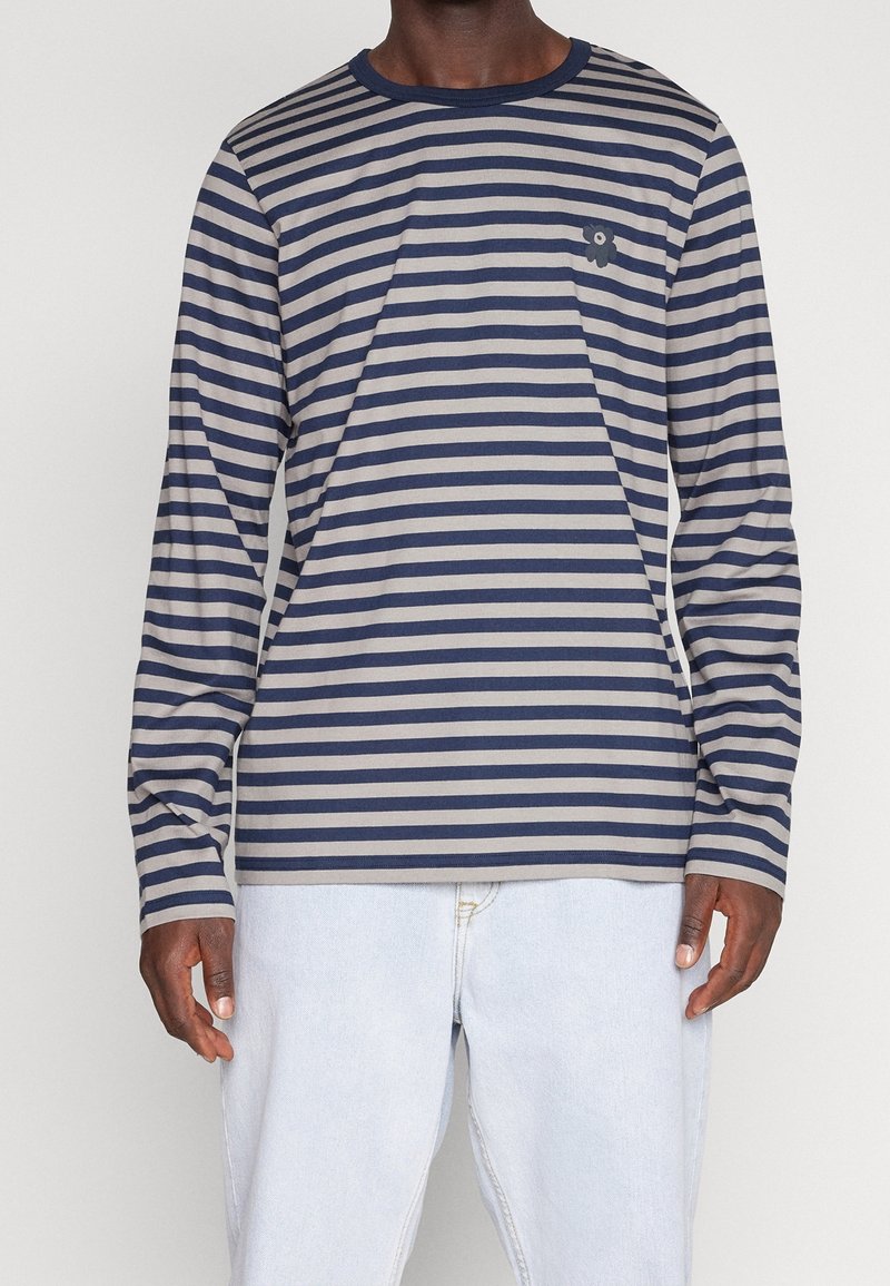 Camisa de manga larga a rayas con rayas en azul marino y gris, cuello redondo y un pequeño emblema en el lado izquierdo del pecho. Fabricada en una tela suave y ligera.