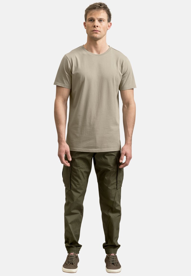 Beige katoenen t-shirt met korte mouwen, gecombineerd met olijfgroene cargo broek met zijzakken en elastische boorden, gedragen met bruine sneakers.
