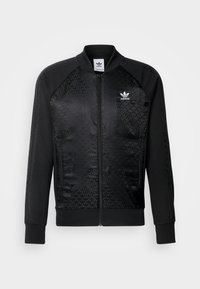 Svart bomberjacka med dragkedja, med en strukturerad framdel med geometriska mönster, ärmar i kontrasterande tyg och en liten vit logotyp på bröstet.