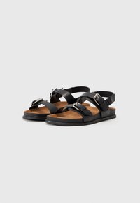 Zwarte sandalen met twee verstelbare banden, zilveren gespen en een gevoerde tan-kleurige voetbed. Platte zool en eenvoudig ontwerp voor comfort.