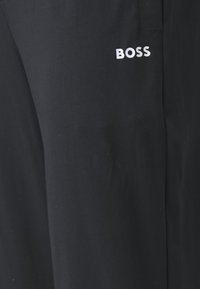Melnas bikses, izgatavotas no gludas auduma, ar baltu "BOSS" logo augšējā kreisajā kājā, taisna griezuma, bez papildu rakstiem vai detaļām.