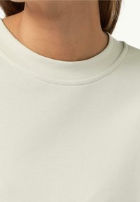 Close-up van een persoon die een effen wit shirt met ronde hals draagt, met de nadruk op de nek en het bovenste deel van de borst.