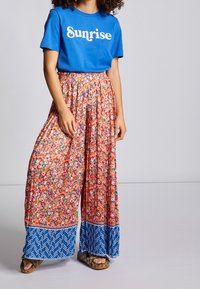 Camiseta azul con el texto "Sunrise", combinada con pantalones palazzo sueltos y estampados con un diseño floral y un borde de espiga azul.