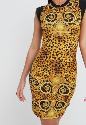 Dopasowana sukienka bez rękawów w panterkę z ozdobnymi złotymi wzorami barokowymi na czarnym tle, noszona przez stojącą osobę.