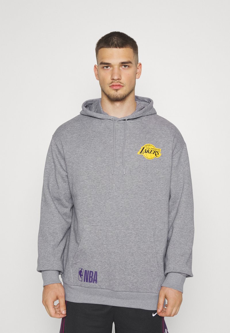 Sudadera gris hecha de tela suave, con un logo de Los Angeles Lakers en amarillo en el pecho y un logo de la NBA en púrpura cerca del dobladillo.