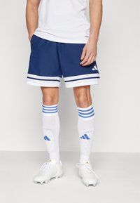 Marineblauwe sportshorts met witte strepen, gecombineerd met witte sokken met blauwe strepen en accenten. Witte voetbalschoenen maken de outfit compleet.
